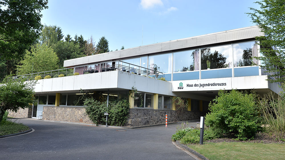Weißes Gebäude 'Haus des Jugendrotkreuzes' des DRK in Bad Münstereifel, umgeben von Büschen und Rasenflächen.